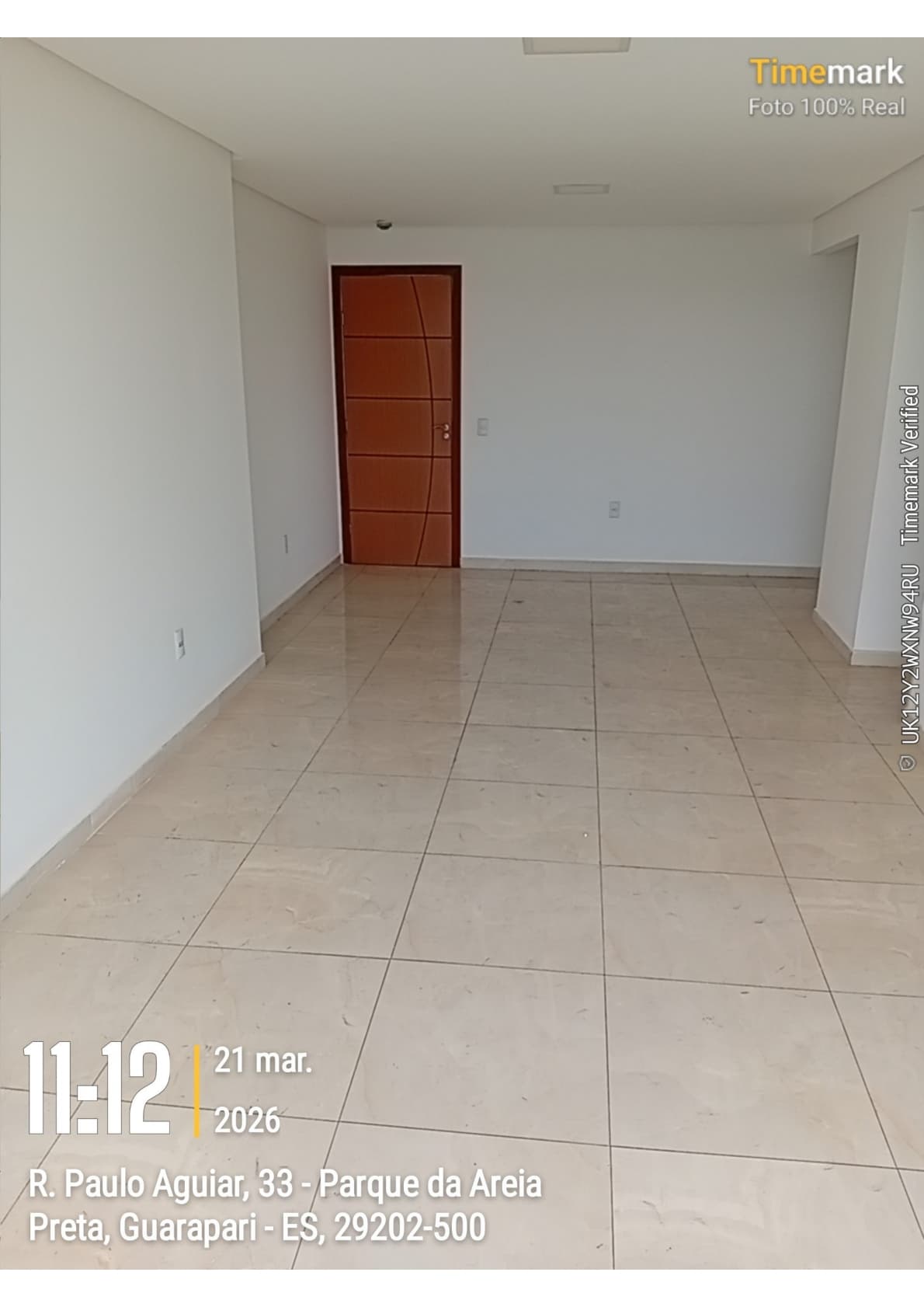 Sala ampla e vazia com piso em porcelanato claro e porta de madeira